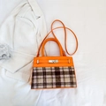 Détail du cuir orange et du tissu à carreaux avec fermoir rotatif argenté sur le sac - Orange