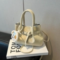 Pale yellow matte bucket bag with crossbody strap and plush animal charm on a white book - White With Pendant
