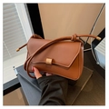 Detalle de bolso bandolera de cuero caramelo con solapa asimétrica y hebilla dorada - Marrón