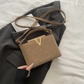 Bolso tipo cubo caqui con herrajes en V dorados y correa ajustable sobre un traje - Caqui