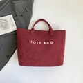 Dunkelrote Tote-Tasche in Wildlederoptik mit weißem Text und zylindrischen Griffen - Rot
