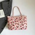 Bolso tote rosa con estampado de cerezas y asas largas sobre traje gris y libro de arte - Rosa