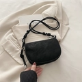 Borsa a sella nera opaca con tracolla regolabile posata su un blazer color beige - Nero