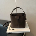 Deep brown suede bucket bag with top handle and adjustable shoulder strap on a prop book - No Pendant / Brown
