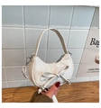 Detail der weißen glänzenden Ledertasche mit Schleife und silbernem Metallanhänger - Weiß