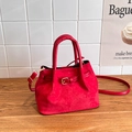 Red vintage bucket bag in faux suede with gold buckle, placed on a wooden table - Red