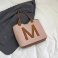 Pink woven tote bag with brown M letter patch and dark trim in a stylish top-down view - Pink