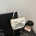 Elegant cream bow handbag with pearl handle and gold chain strap on black background - White