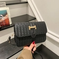 Bolso bandolera tejido negro con hebilla H dorada llevado por modelo en un ambiente moderno - Negro