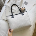 Beige woven tote bag with black leather straps on a soft bed for casual daily commute - White