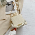 Bolso saco crema con asa de perlas y textura ondulada en un ambiente elegante - Blanco