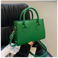 Close-up of small emerald green leather handbag with gold hardware on a black leather chair - Green
