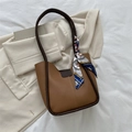 Brown leather bucket bag with dark trim and silk scarf on a white textile background - Brown