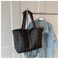 Detail of black quilted down tote bag hanging next to a denim jacket in indoor setting - Black