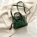 Mini sac bandoulière vert foncé à texture crocodile et logo sur fond de veste beige - Vert