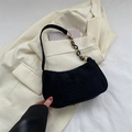 Black quilted baguette bag with metal chain strap displayed on a cream blazer - Black