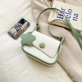 Borsa a sella beige chic con bordo verde e ciondolo a fiore per donna in un set lifestyle - Verde