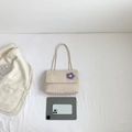 Creamy white woven straw shoulder bag with purple knit flower on white background - Beige