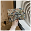 Detail einer floralen Jacquard-Umschlagtasche mit goldener Kleeblatt-Schließe im Alltag - Kleines Blaues Blümchen