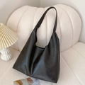 Minimalist large black faux leather tote bag on beige sofa for a modern chic look - Black