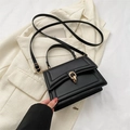 Bolso de mano minimalista negro con hebilla dorada sobre fondo de chaqueta beige - Negro