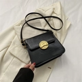 Bolso bandolera negro vintage con hebilla circular dorada sobre traje blanco - Negro