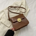 Bolso bandolera de cuero marrón vintage con hebilla dorada sobre una chaqueta blanca - Marrón