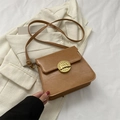 Bolso bandolera vintage de cuero marrón con cierre retro sobre una chaqueta crema - Caqui