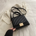 Chic black tote bag with vertical pleats and golden clasp on beige suit backdrop - Black