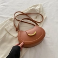 Braune Leder-Satteltasche in Halbmondform mit goldener Sichelschließe auf Stoff - Braun