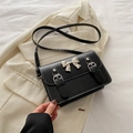 Piccola borsa a tracolla nera con fiocco argento su sfondo di una giacca beige - Nero