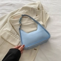 Bolso hobo azul claro minimalista con cadena a juego sobre un fondo de blazer elegante - Azul