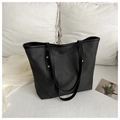 Bolso tote negro minimalista con remaches dorados sobre fondo textil blanco suave - Negro