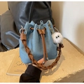 Detalle de bolso saco de mezclilla azul con asa trenzada marrón y colgante de monstruo - Azul