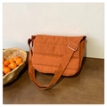 Detail of warm orange quilted crossbody bag with adjustable wide shoulder strap on wooden desk - Orange