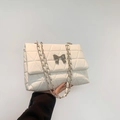 White quilted crossbody bag with silver bow accent and elegant chain strap detail - White