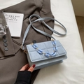 Sac à main matelassé bleu clair avec chaîne dorée sur fond de veste marron - Bleu