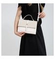 Detail of cream white handbag with woven texture flap and golden buckle worn by model - White