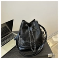Detail of a chic bucket bag with silver chain drawstring and leather splicing on a desk - Black