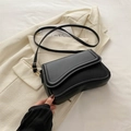 Borsa a spalla nera in pelle con patta curva poggiata su una giacca color crema - Nero