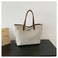 Detalle de un bolso tote de lona minimalista con asas de cuero marrón y placa de metal plateado - café