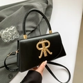 Schwarze Retro-Umhängetasche aus Leder mit goldenem R-Logo und Krone vor grauem Anzug - Schwarz