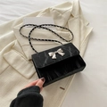Chique zwarte crossbodytas met zilveren strikgesp en elegante kettingriem op witte blazer - Zwart