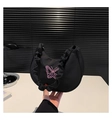 Detail of a black pleated crescent bag featuring pink butterfly embroidery on a white desk - Black