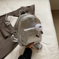 Schicker silberner Metallic-Minirucksack mit flauschigem Anhänger auf weißem Bett - Mit Anhänger / Silber