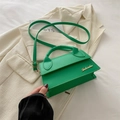 Elegante borsa a tracolla verde minimalista con logo dorato posata su un blazer - Verde