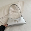 Bolso baguette plateado con lazo metálico sobre fondo de blazer beige chic - Plateado