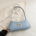Bolso de hombro baguette azul claro con hebilla de lazo plateada sobre fondo blanco texturizado - Azul