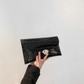 Schwarze Clutch mit Krokodilprägung und silberner Herzschließe in der Hand gehalten - Schwarz