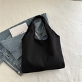 Minimalist black canvas tote bag with seamless handle on a textured white fabric backdrop - Black